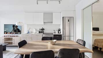 A modern kitchen with white cabinets, a stainless steel refrigerator, and a dining area with a wooden table and black chairs.
