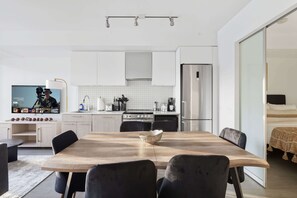 A modern kitchen with white cabinets, a stainless steel refrigerator, and a dining area with a wooden table and black chairs.