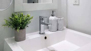 A bathroom with a white sink, a chrome faucet, a potted plant, and two marble containers.