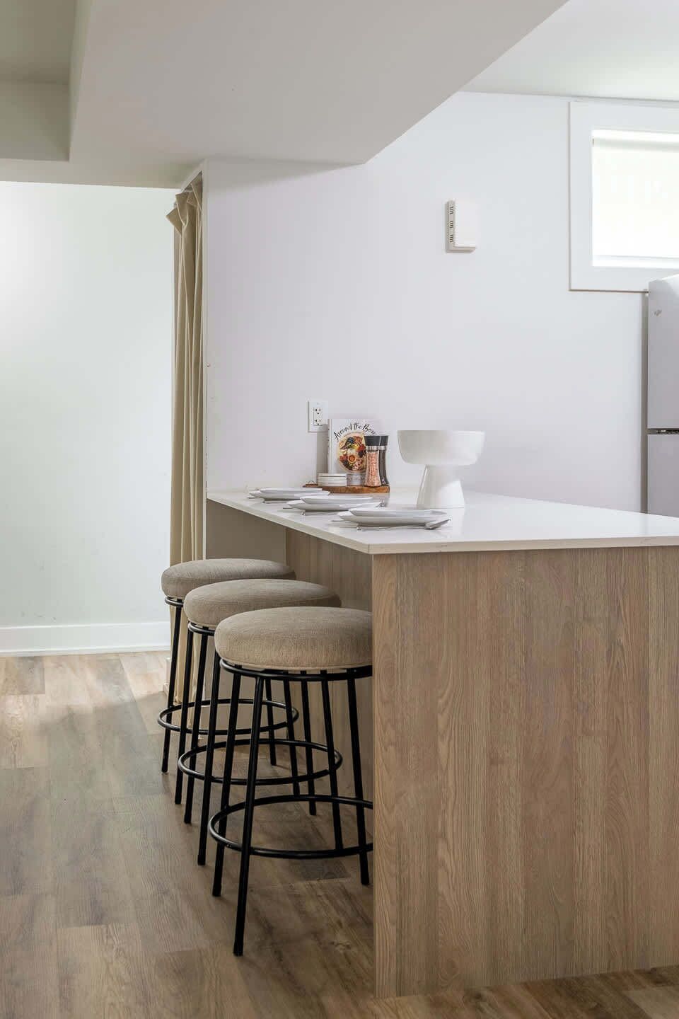 A kitchen with a wooden island, bar stools, and a white countertop.