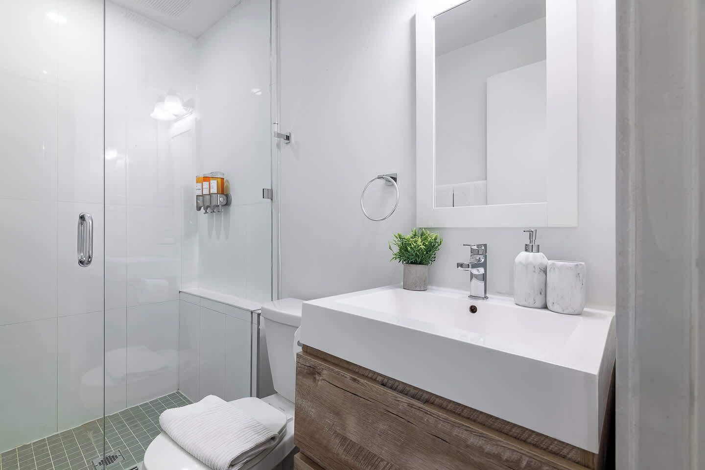 A modern bathroom with a glass shower enclosure, a white sink with a marble countertop, and a wooden vanity.