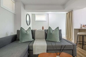 Ein modernes Wohnzimmer mit grauem Sofa, einem kleinen Holztisch und einem Spiegel an der Wand.