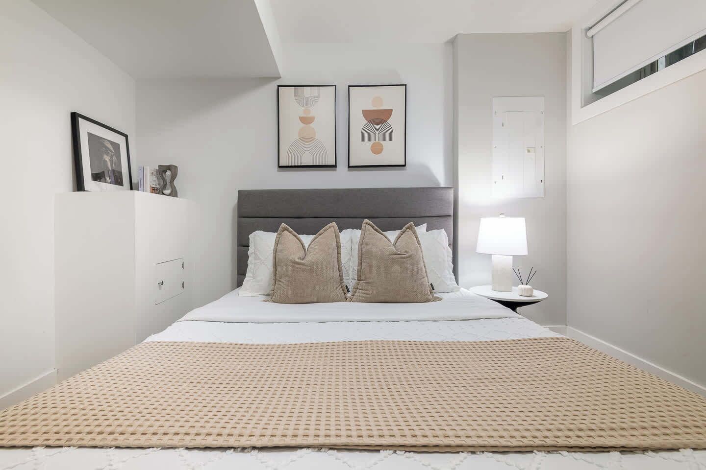 Une chambre à coucher avec un lit, des oreillers, une table de chevet avec une lampe et des œuvres d’art murales.