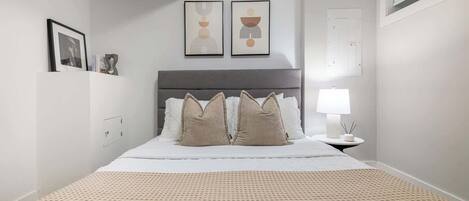 Une chambre à coucher avec un lit, des oreillers, une table de chevet avec une lampe et des œuvres d’art murales.