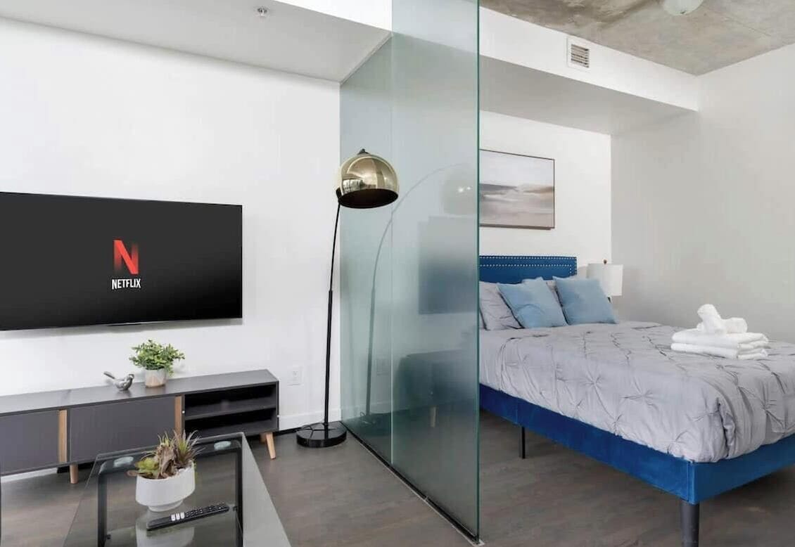 Un dormitorio moderno con una cama, un televisor montado en la pared y un panel de vidrio.