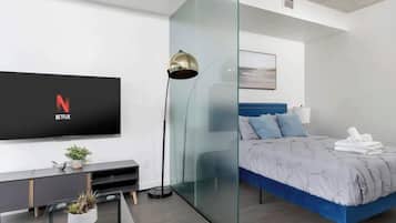 Un dormitorio moderno con una cama, un televisor montado en la pared y un panel de vidrio.