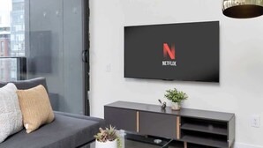 Un salon moderne avec un canapé, une table basse en verre, un téléviseur fixé au mur et un luminaire suspendu.