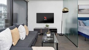 Un salon moderne comprenant un canapé, une table basse, un téléviseur fixé au mur et un lit séparé par une cloison en verre.
