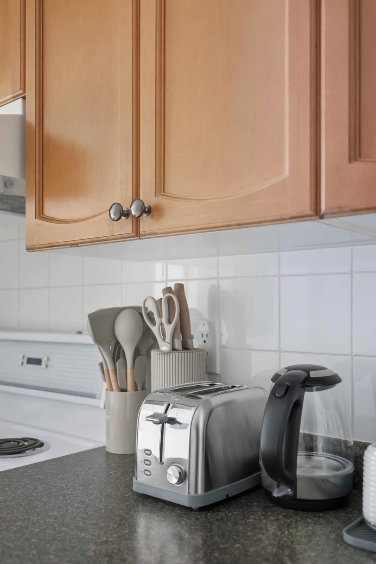 A kitchen with wooden cabinets, a toaster, a kettle, and a utensil holder.