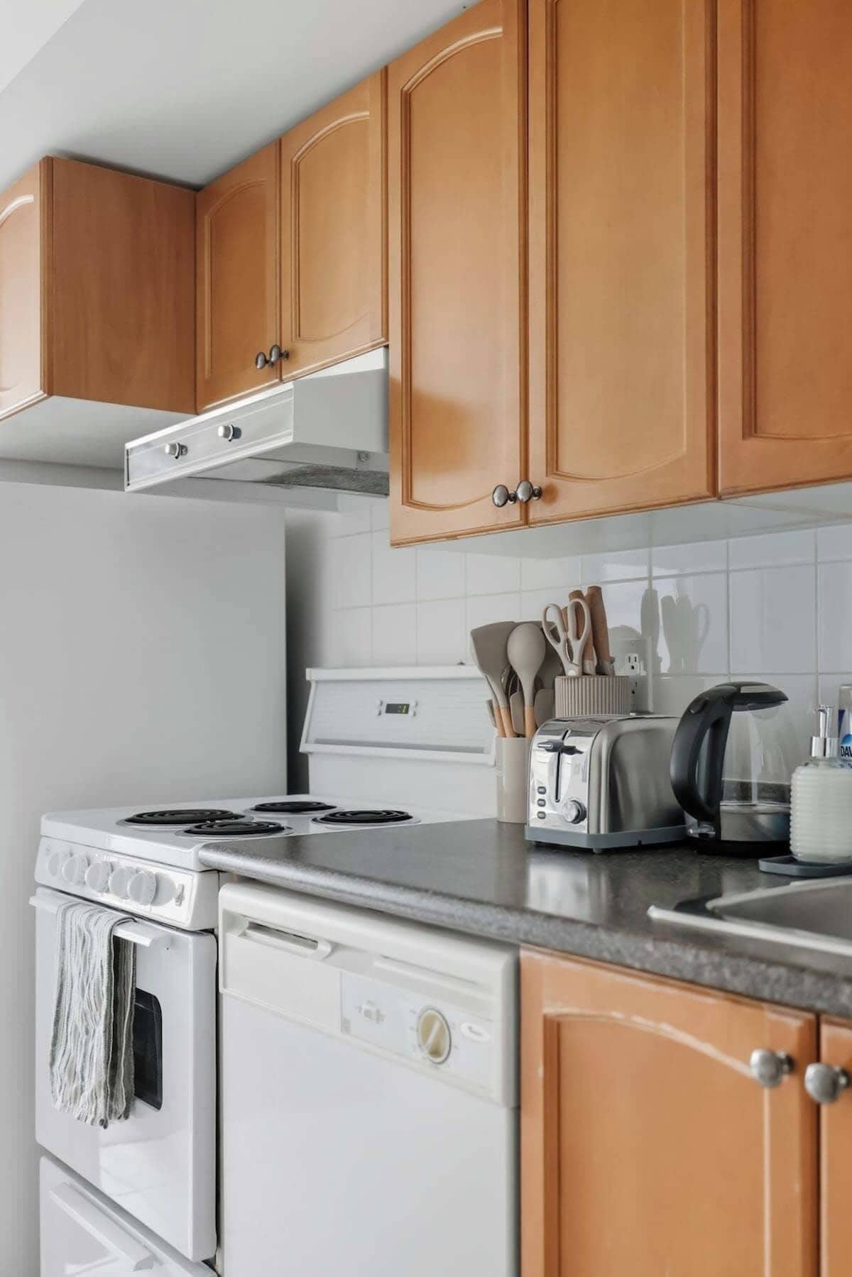 A kitchen with wooden cabinets, a white stove, a dishwasher, and a toaster on the countertop.