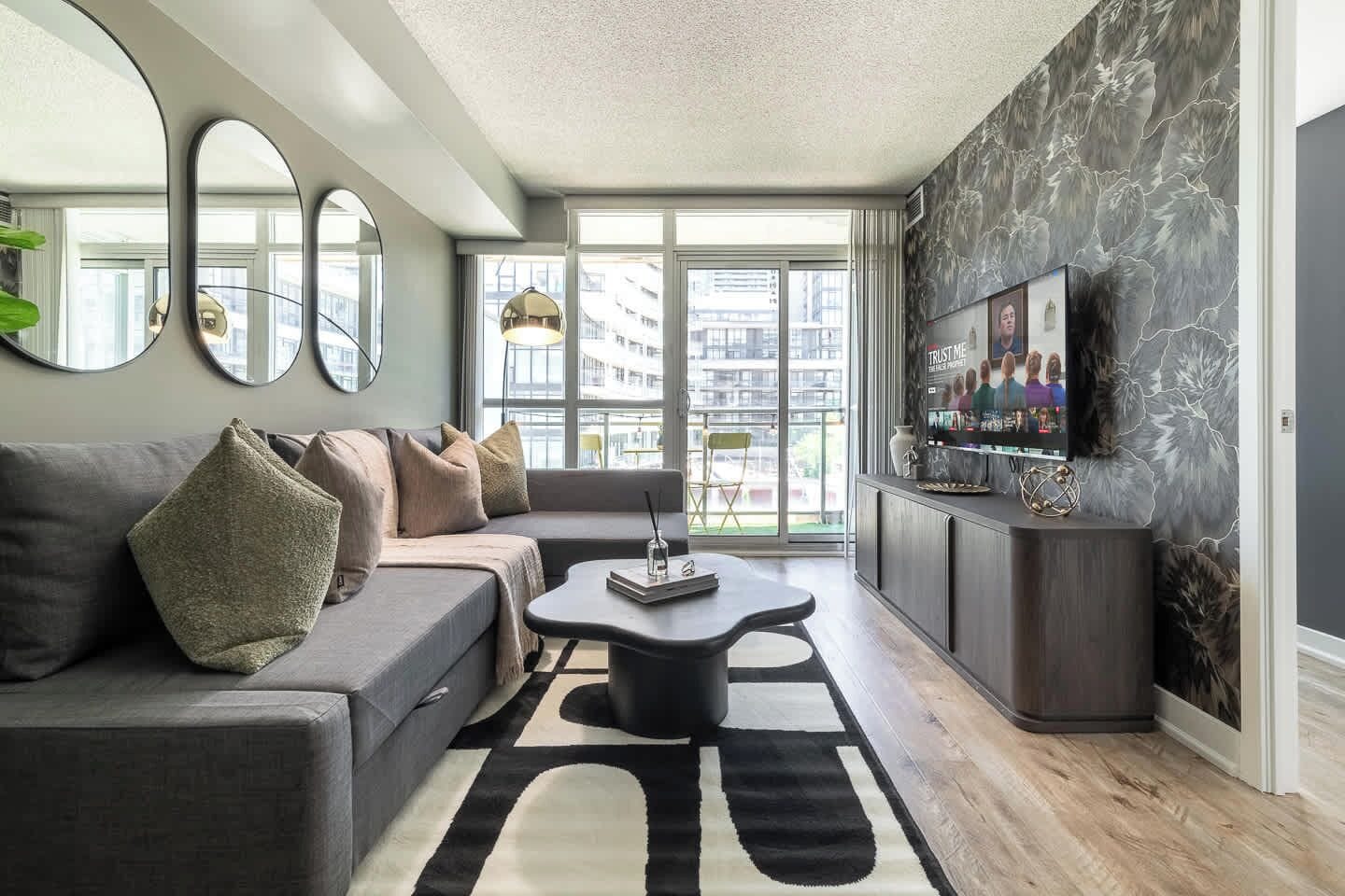 A modern living room with a grey sofa, a coffee table, and a TV on a wall with a floral pattern.