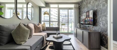 A modern living room with a grey sofa, a coffee table, and a TV on a wall with a floral pattern.