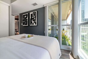 A modern hotel room with a large bed, a balcony with a yellow chair, and a city view. - Downtown Skyline 2BR+Den Oasis w/ Parking  | Parking Available (Toronto)