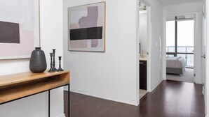 A modern interior with a hallway leading to a bedroom. There is a console table with a vase and candle holders. A framed abstract painting is on the wall. - Above the City Designer Sub-Penthouse Oasis (Toronto)