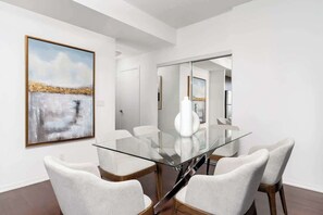 A modern dining room with a glass table, white chairs, and a large abstract painting on the wall.