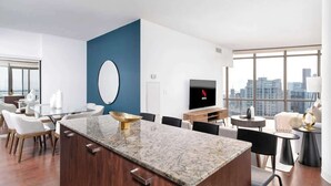 A modern living room with a large window, a flat-screen TV, and a dining area with a marble island. - Above the City Designer Sub-Penthouse Oasis (Toronto)