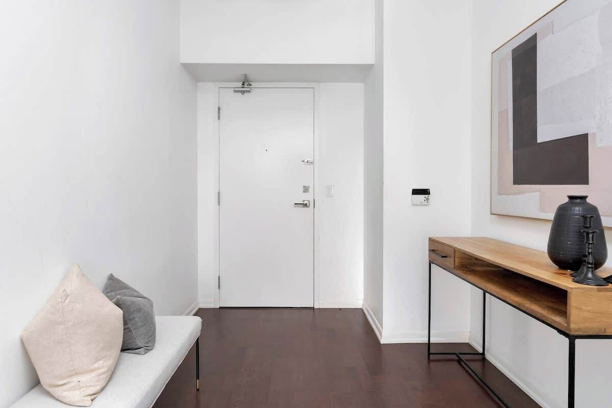 A hallway with a white door, a wooden console table with a vase, and a grey sofa with cushions.