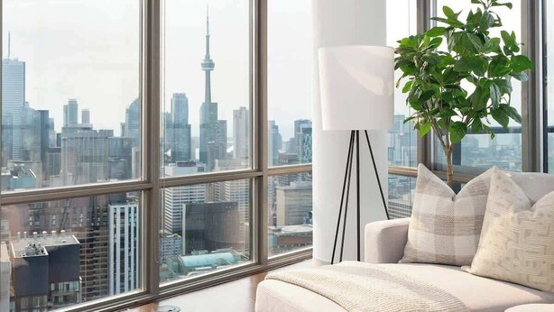 A modern living room with a large window, a white sofa, a floor lamp, and a potted plant. - Above the City Designer Sub-Penthouse Oasis (Toronto)