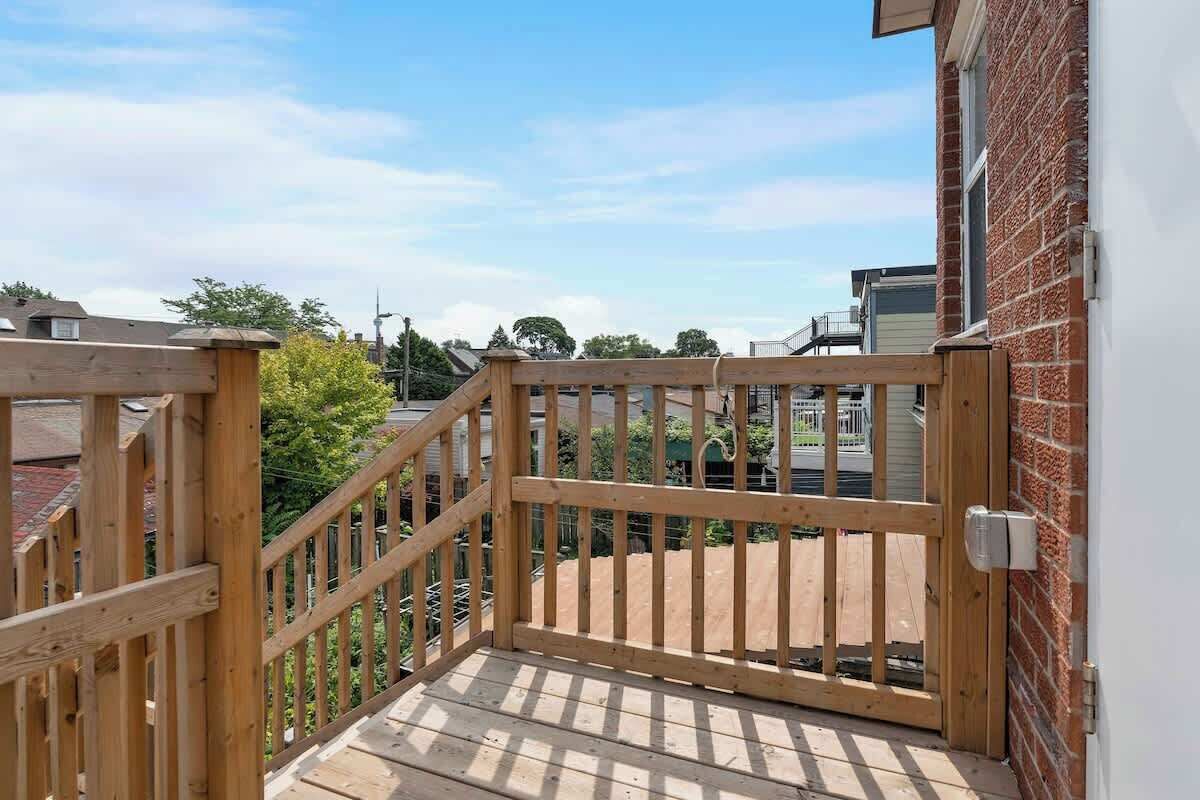 A wooden deck with a gate leading to a brick wall, surrounded by greenery and other buildings.