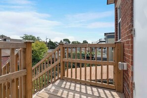 A wooden deck with a gate leading to a brick wall, surrounded by greenery and other buildings.