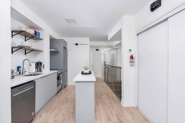 A modern kitchen with white cabinetry, a central island, and a black railing along the hallway.