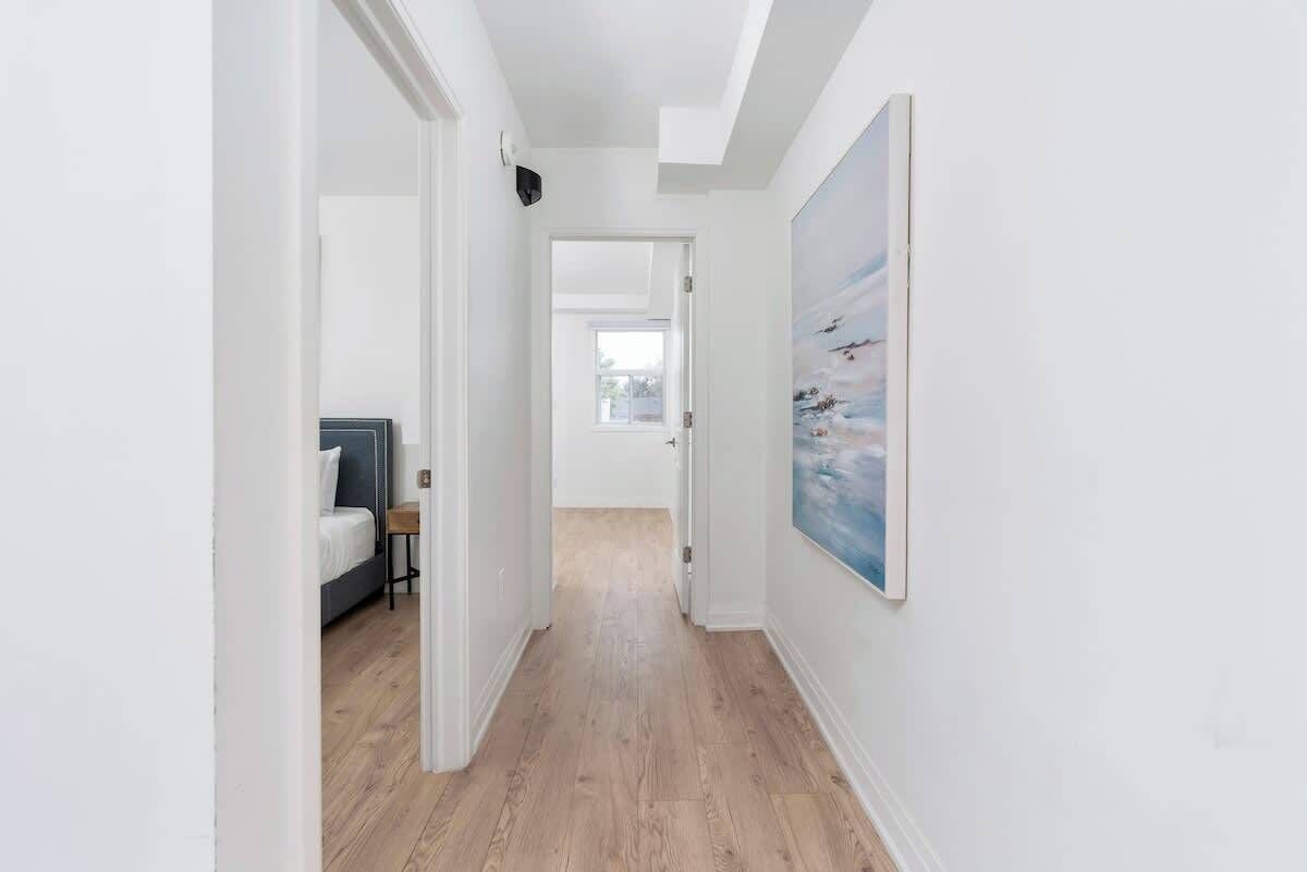 A hallway with a bed, a painting, and a door leading to another room.