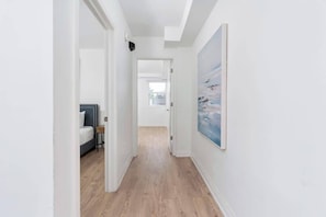 A hallway with a bed, a painting, and a door leading to another room.
