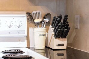 Una cocina con estufa blanca, un portalapiedras identificado como 'UTENSILS' y un bloque para cuchillos con la marca 'TERRIWARE'.