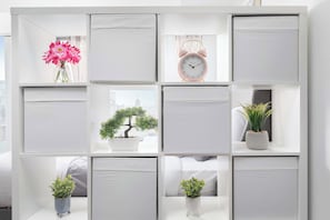 Une étagère blanche contenant divers objets, notamment une horloge, un bonsaï et des plantes en pot.