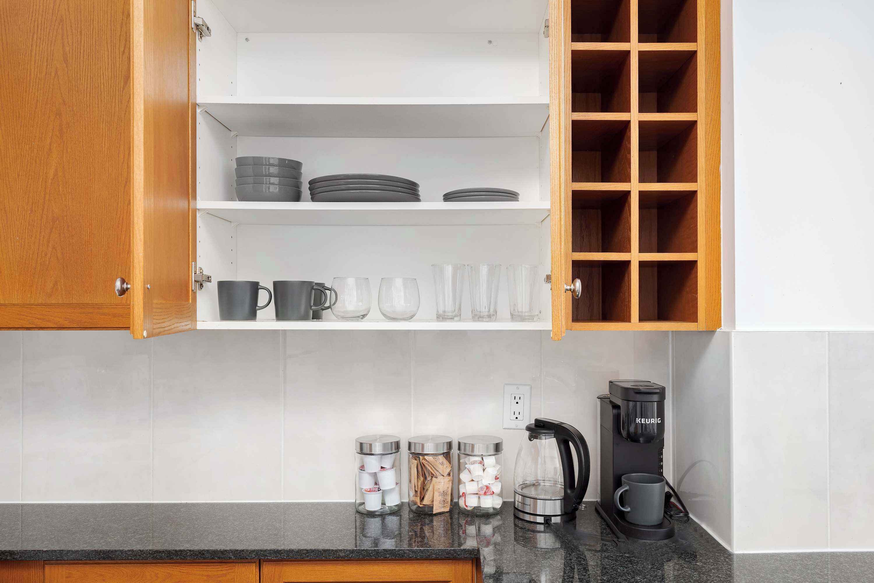 A kitchen with open cabinets, a coffee maker, and storage jars.