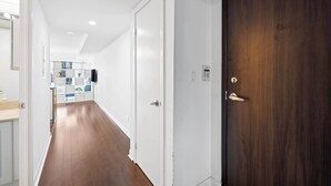 A hallway with a wooden floor, white walls, and a dark wooden door with a keypad lock.