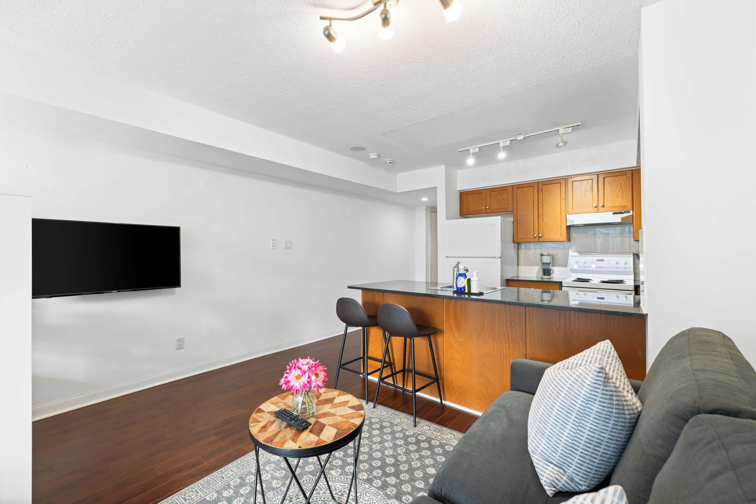 A modern living room with a sofa, a coffee table with a vase, and a TV mounted on the wall.