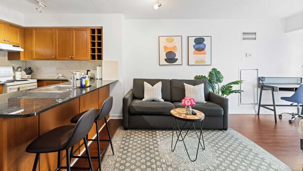 A modern kitchen with wooden cabinets, a central island, and a dining area with a sofa and coffee table.