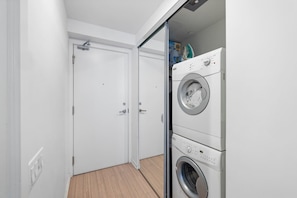 A laundry room with a front-loading washer and dryer, a door, and a wooden floor.