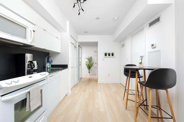 A modern kitchen with white cabinetry, a stove, and a dining area with black chairs and a table. - Cozy Toronto Stay Skyline View | Parking Available (Toronto)