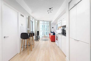 A modern kitchen with white cabinets, a red sofa, and a dining area with a black chair and a small table. - Cozy Toronto Stay Skyline View | Parking Available (Toronto)