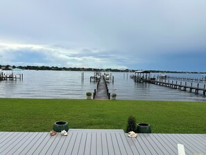 A waterfront property with a wooden deck, a dock extending into the water, and a grassy area in the foreground. - Historic waterfront 4-bedroom, 2 bath house on St Lucie River-Big Water Views (Stuart)