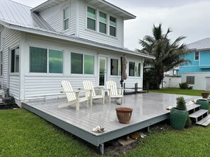 Una casa blanca con un porche cubierto, dos sillas Adirondack y una mesa de patio.