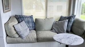 A room with a beige sofa, striped pillows, a marble table, and a window with a view of greenery. - Historic 4-bedroom/2 bath house on St Lucie River-Big Water Views (Stuart)