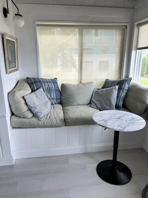 A room with a beige sofa, striped pillows, a marble table, and a window with a view of greenery. - Historic 4-bedroom/2 bath house on St Lucie River-Big Water Views (Stuart)