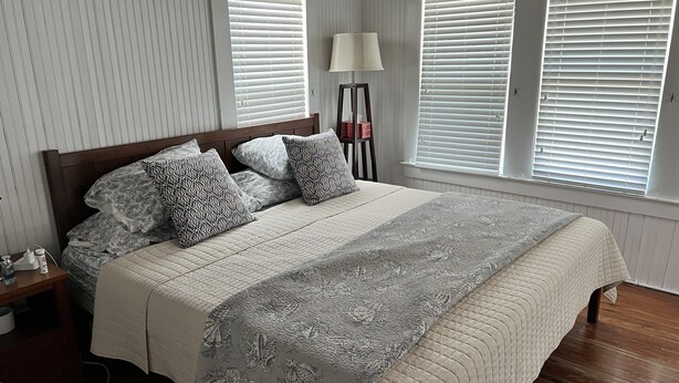 A bedroom with a bed, bedside table, lamp, and windows with blinds. - Historic 4-bedroom/2 bath house on St Lucie River-Big Water Views (Stuart)