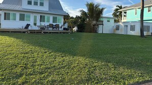 A residential area with a grassy lawn, a white house with a balcony, and a blue house in the background. - Historic 4-bedroom/2 bath house on St Lucie River-Big Water Views (Stuart)