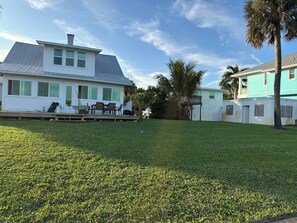 A residential area with a grassy lawn, a white house with a balcony, and a blue house in the background. - Historic 4-bedroom/2 bath house on St Lucie River-Big Water Views (Stuart)
