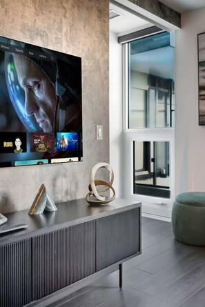 Un salón moderno con un televisor de pantalla plana grande montado en una pared texturizada, una mesa consola contemporánea y un ventanal con vistas al exterior.