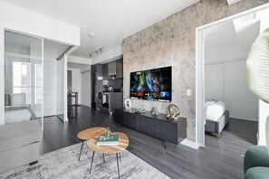 Una sala de estar moderna con un televisor de pantalla plana grande montado en una pared texturizada, un sofá, una mesa de centro y una cocina al fondo.