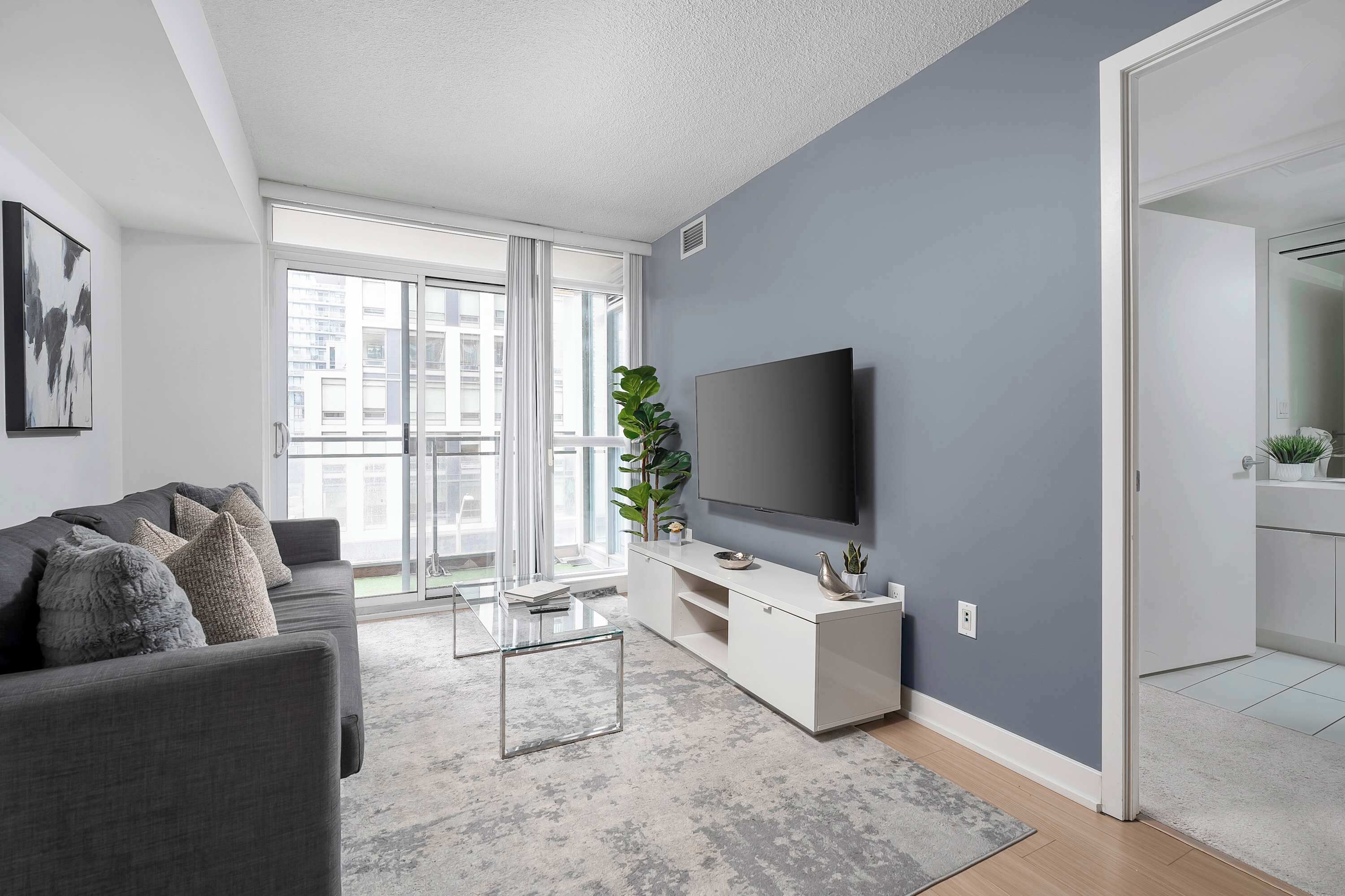 Un salon moderne avec un canapé gris, une table basse en verre, un téléviseur à écran plat et un mur d’accent de couleur grise.