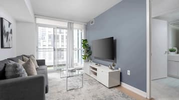 A modern living room with a grey sofa, a glass coffee table, a flat-screen TV, and a grey accent wall.