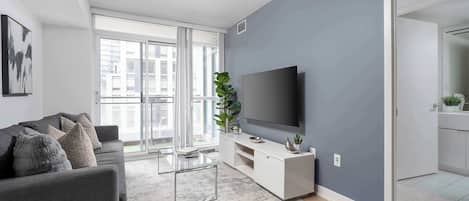 Una sala de estar moderna con un sofá gris, una mesa de centro de vidrio, un televisor de pantalla plana y una pared de acento gris.