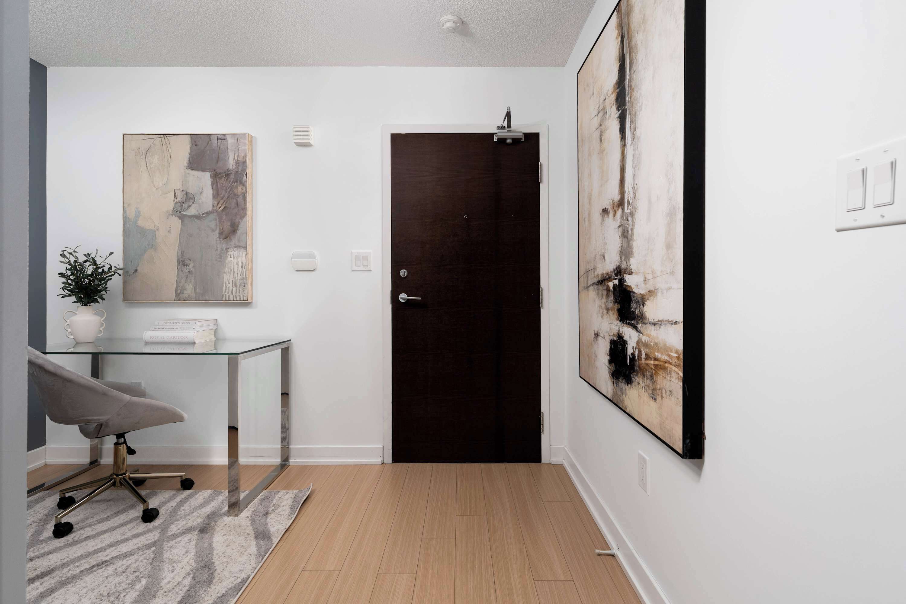 A modern interior with a glass desk, a dark door, and abstract art on the walls.