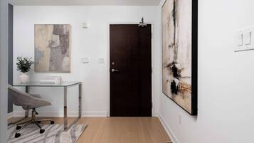 A modern interior with a glass desk, a dark door, and abstract art on the walls.